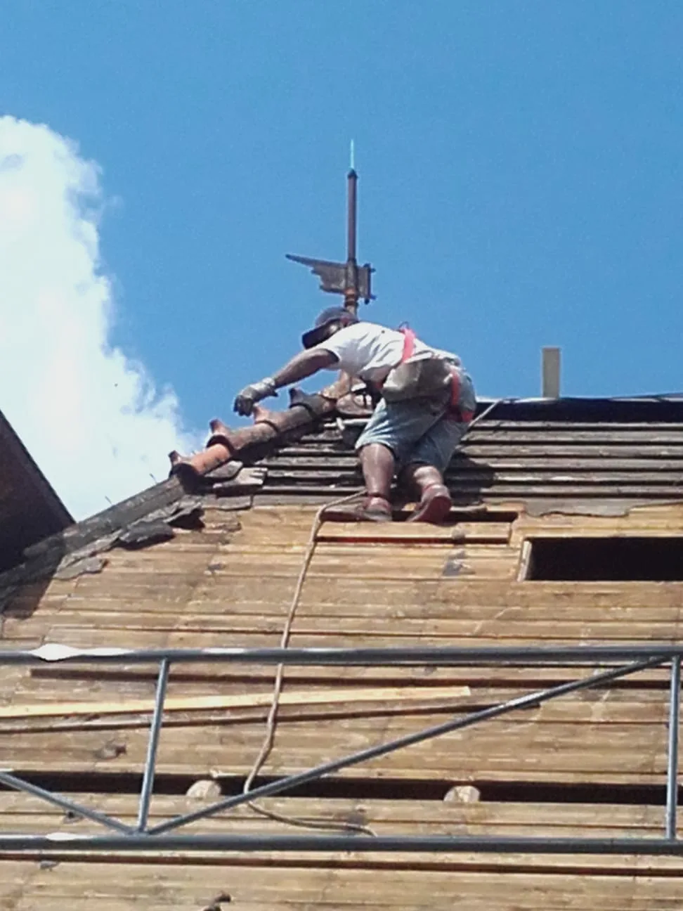 Dachdecker arbeitet am First eines alten Daches, oben eine Wetterfahne