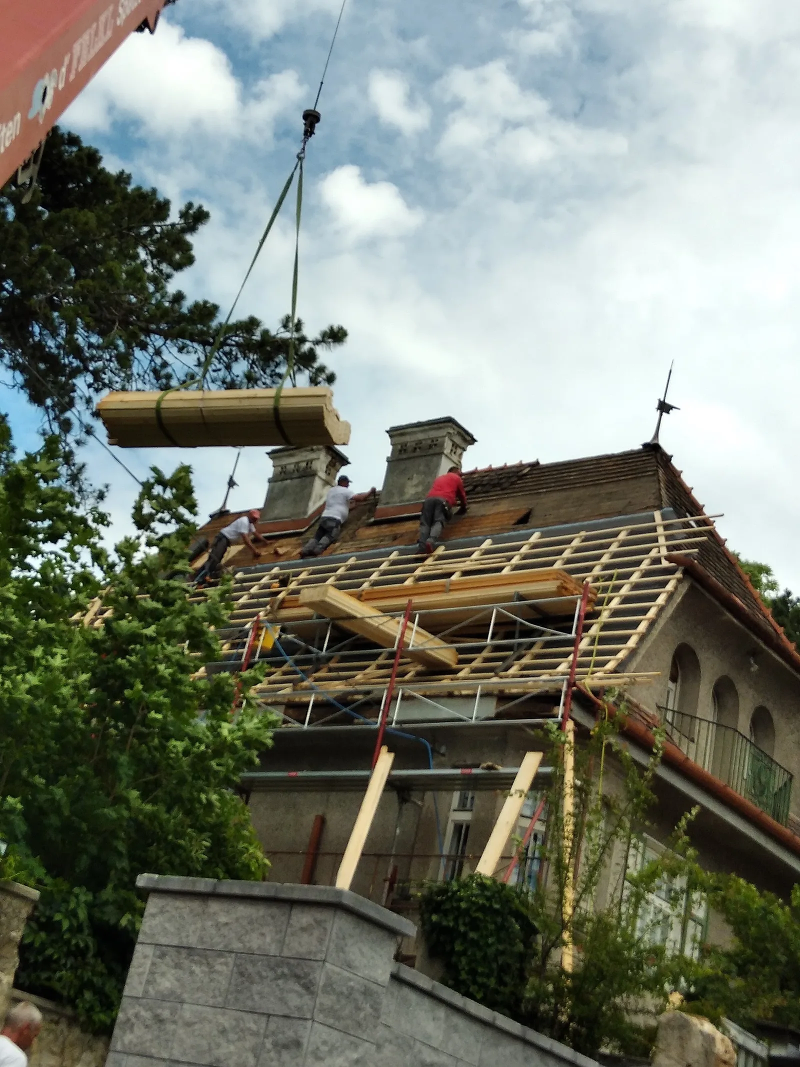 Drei Dachdecker arbeiten auf dem Dach eines alten Hauses, ein Kran hebt eine Last